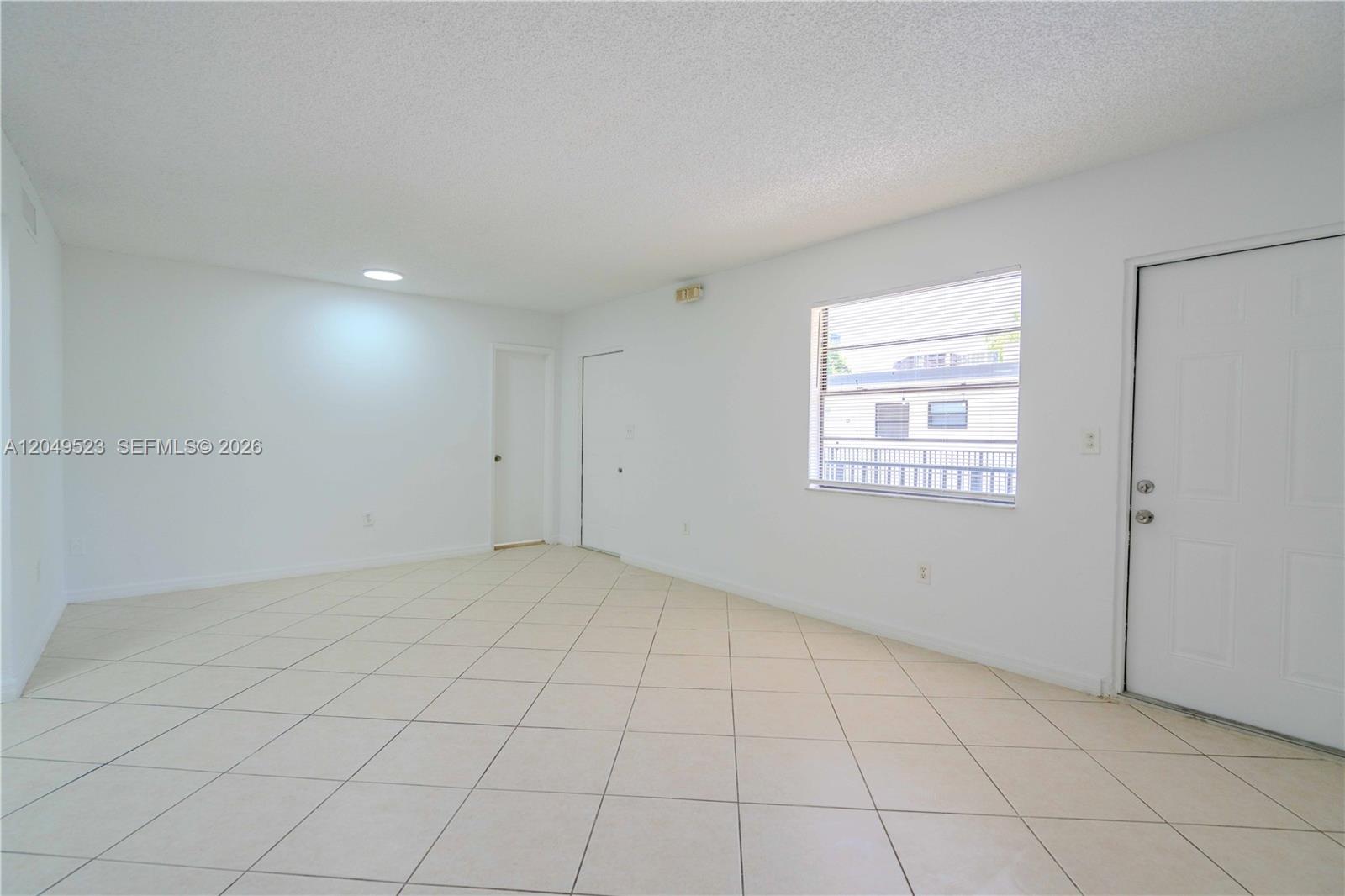 An empty room features white walls, light-colored tile flooring, a window, and two doors — 3265 Virginia St # 15, Miami FL 33133, MIAMI, FL