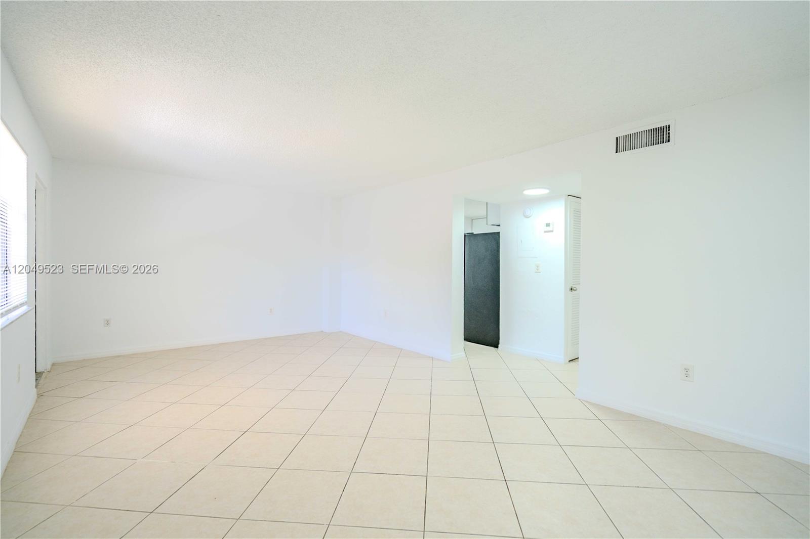 An empty room features white walls, a tiled floor, and a doorway leading to a kitchen — 3265 Virginia St # 15, Miami FL 33133, MIAMI, FL