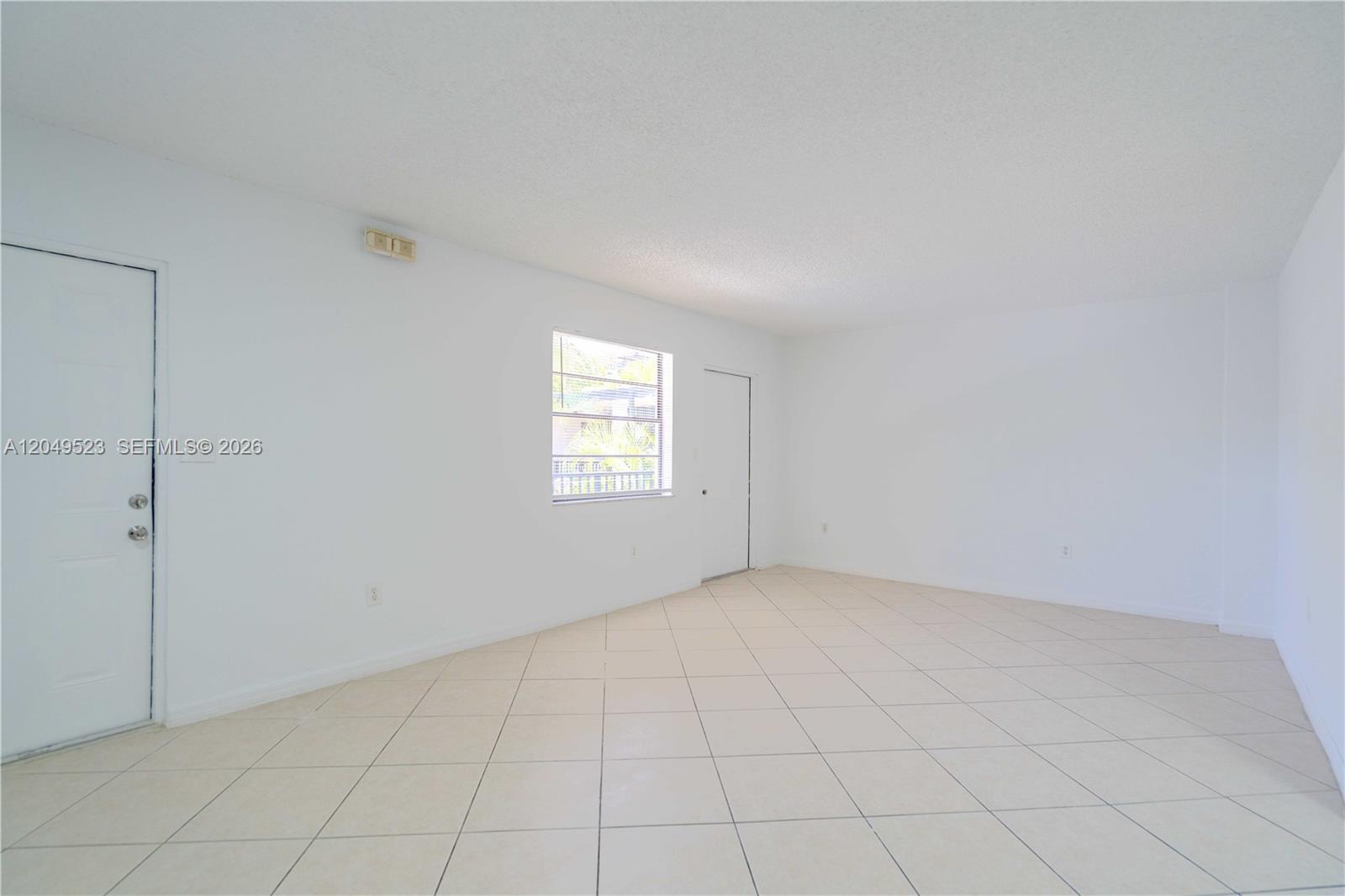 An empty room features white walls, light-colored tile flooring, a window, and two doors — 3265 Virginia St # 15, Miami FL 33133, MIAMI, FL