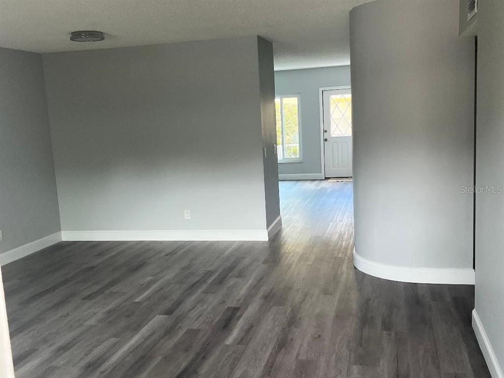 A room with gray walls and wood-look flooring leads to an entryway with a door — 2294 BELGIAN LANE UNIT 14, CLEARWATER, FL