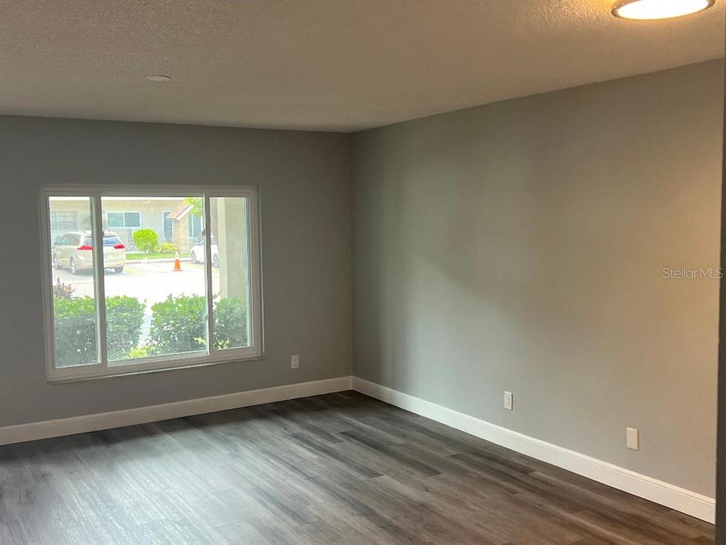 An empty room features gray walls, white trim, and wood-look flooring with a large window — 2294 BELGIAN LANE UNIT 14, CLEARWATER, FL