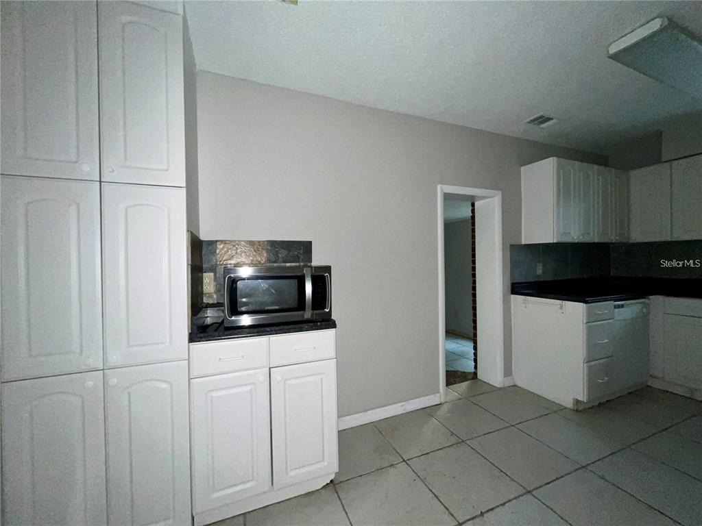 A kitchen features white cabinets, a microwave on a counter, and light-colored tile flooring — 3029 SLEEPY HILL ROAD, LAKELAND, FL