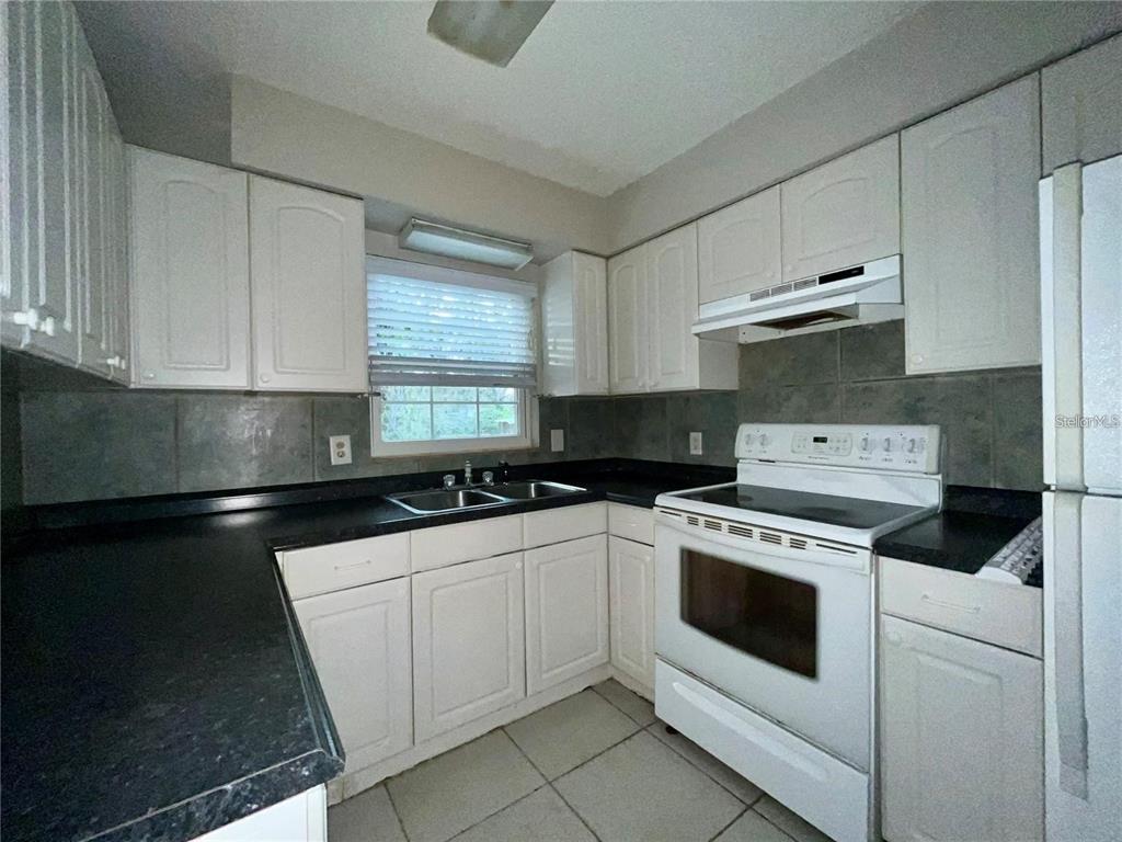 A kitchen features white cabinets, black countertops, a white stove, and a tiled backsplash — 3029 SLEEPY HILL ROAD, LAKELAND, FL