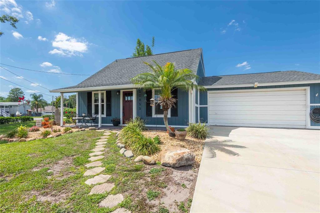 A blue single-story house features a white garage, a stone walkway, and a palm tree — 21855 OCEAN PINES DRIVE, LAND O LAKES, FL