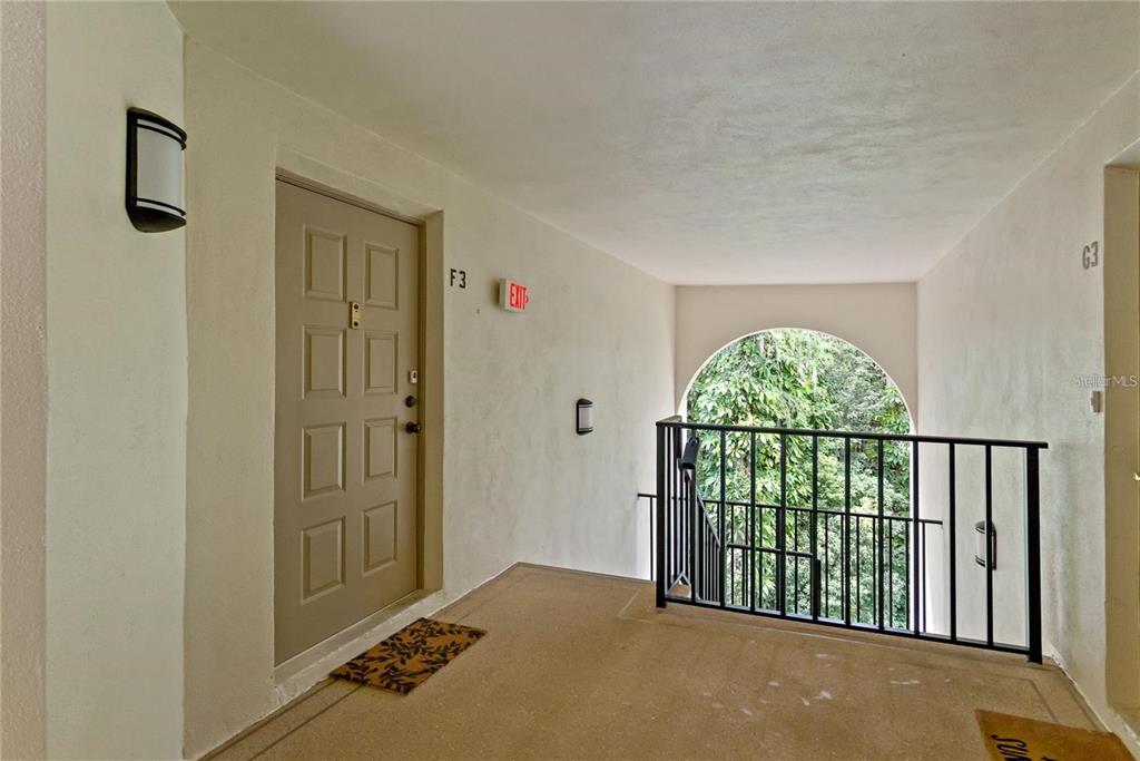 An outdoor apartment hallway features a tan door labeled F3, a railing, and arched opening — 3161 LAKE PINE WAY S UNIT F3, TARPON SPRINGS, FL