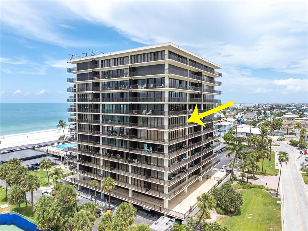 An aerial view of a multi-story beachfront condominium building with a yellow arrow pointing right — 7600 BAYSHORE DRIVE UNIT 701, TREASURE ISLAND, FL