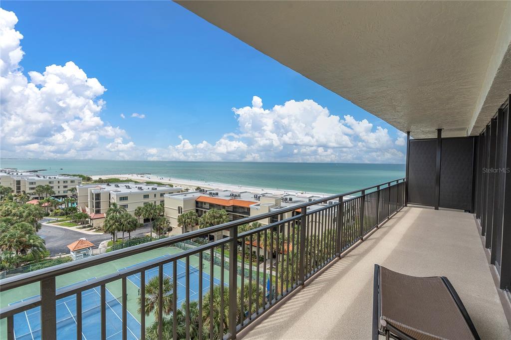 A balcony with a metal railing overlooks a tennis court, beach, and the ocean — 7600 BAYSHORE DRIVE UNIT 701, TREASURE ISLAND, FL