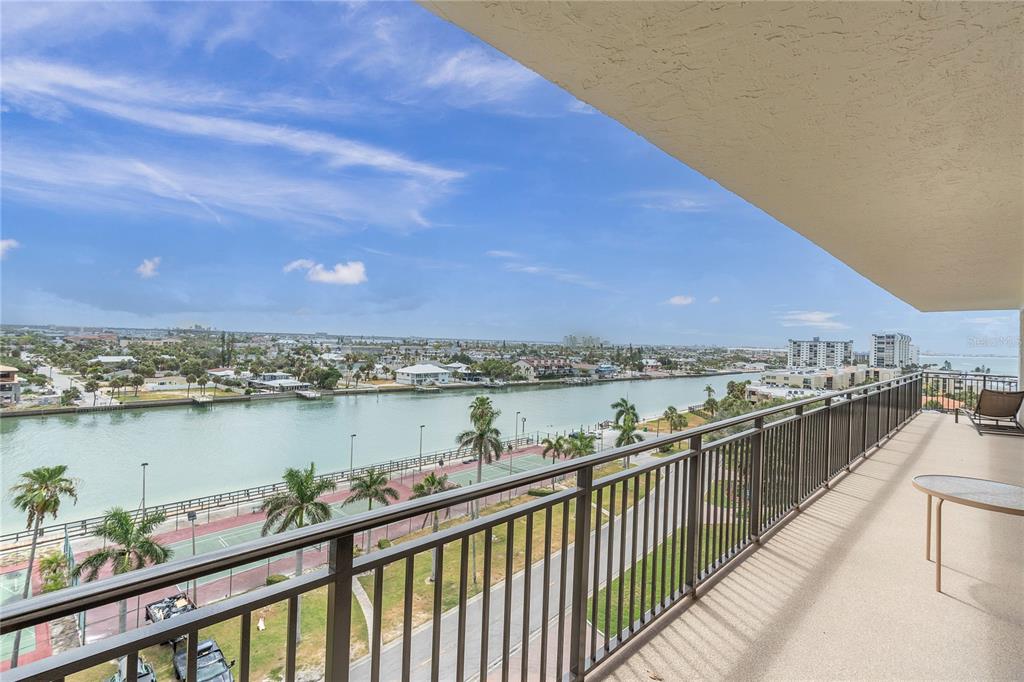 A high-angle view from a balcony overlooking a waterway, tennis courts, and palm trees — 7600 BAYSHORE DRIVE UNIT 701, TREASURE ISLAND, FL