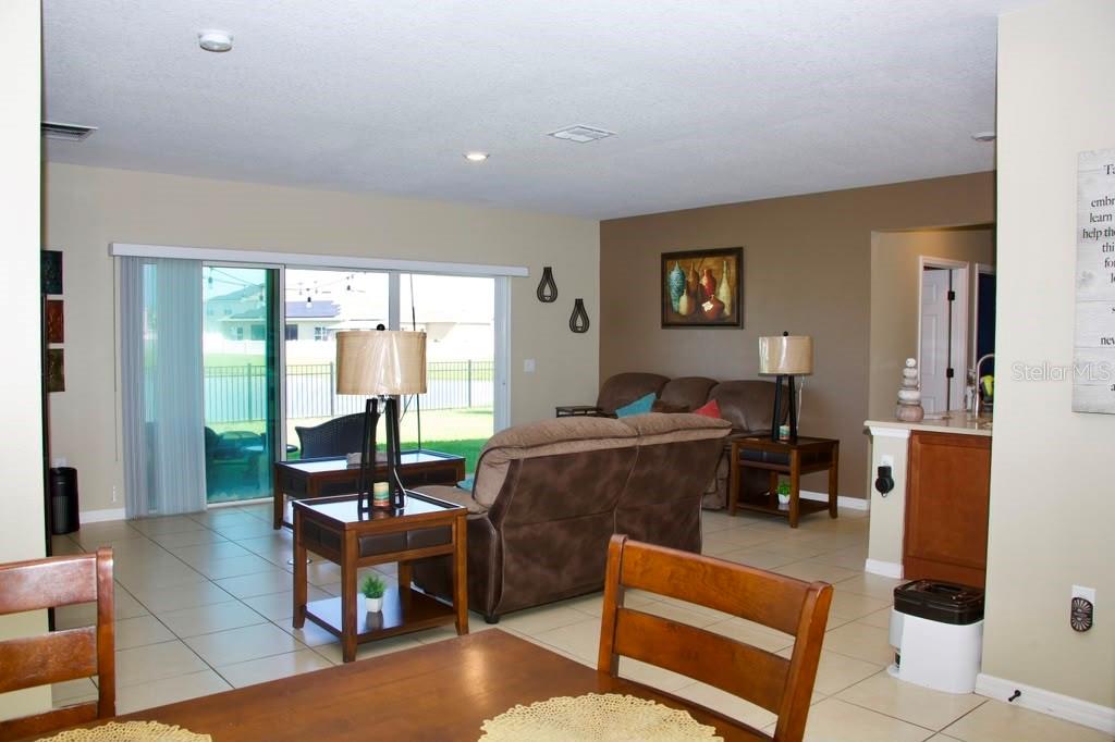 A living room with tile floors, brown furniture, and a sliding glass door to the backyard — 411 BLUE LAKE CIRCLE, KISSIMMEE, FL