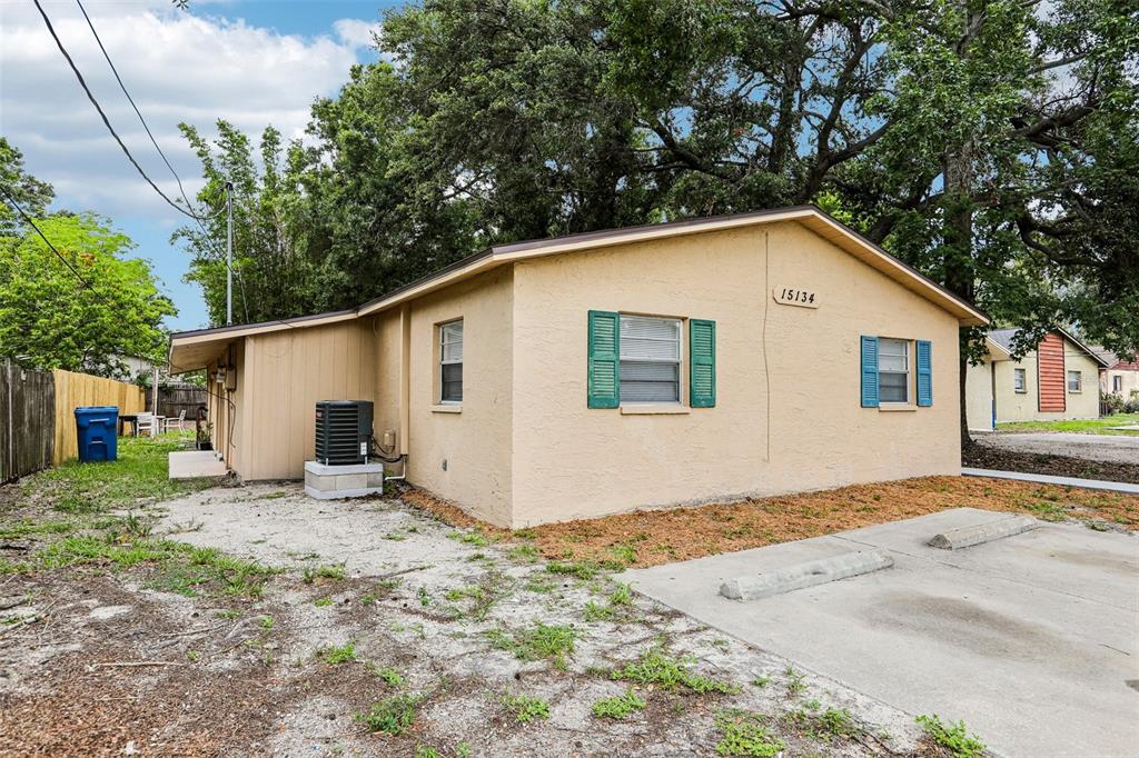A tan, single-story house with green shutters and a concrete parking area in front — 15134 VERONA AVENUE, CLEARWATER, FL