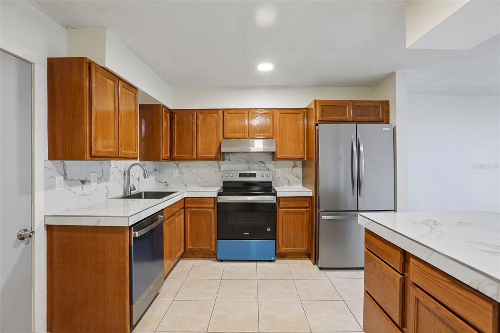 A kitchen features wood cabinets, white marble-look countertops, stainless steel appliances, and tiled flooring — 15134 VERONA AVENUE, CLEARWATER, FL