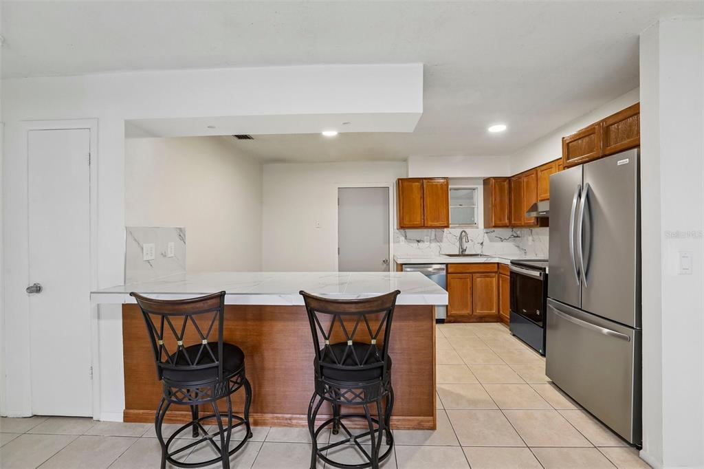 A kitchen features wood cabinets, stainless steel appliances, a marble-look island, and two bar stools — 15134 VERONA AVENUE, CLEARWATER, FL