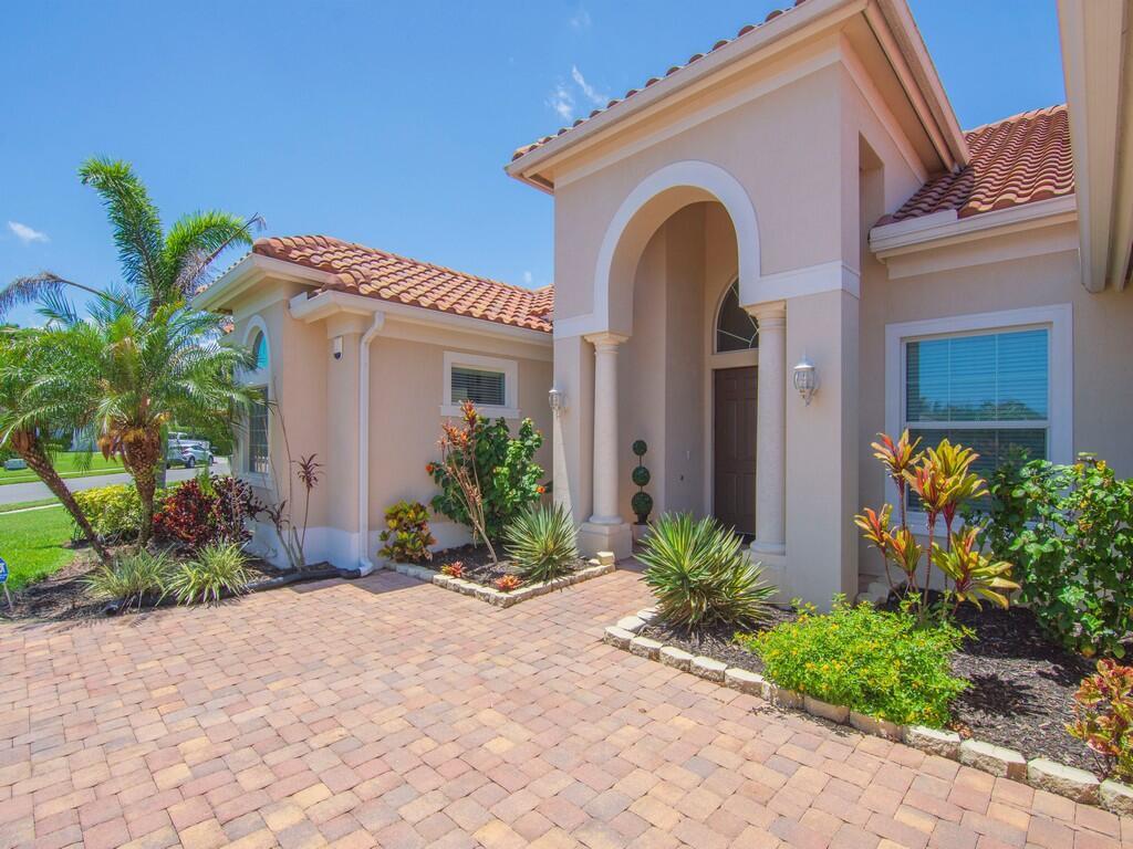 A beige house with a tiled roof features a paved driveway and landscaped front garden — 4405 65th Drive, Vero Beach FL 32967, VERO BEACH, FL