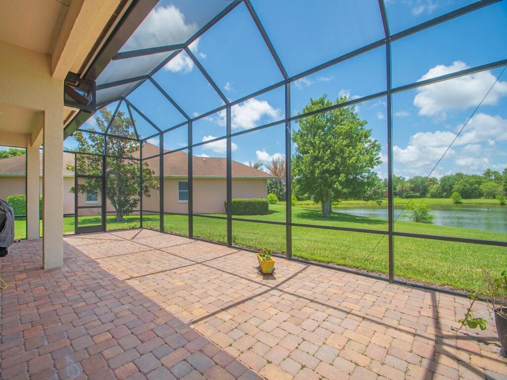 A screened-in patio with brick pavers overlooks a grassy lawn and a small lake — 4405 65th Drive, Vero Beach FL 32967, VERO BEACH, FL