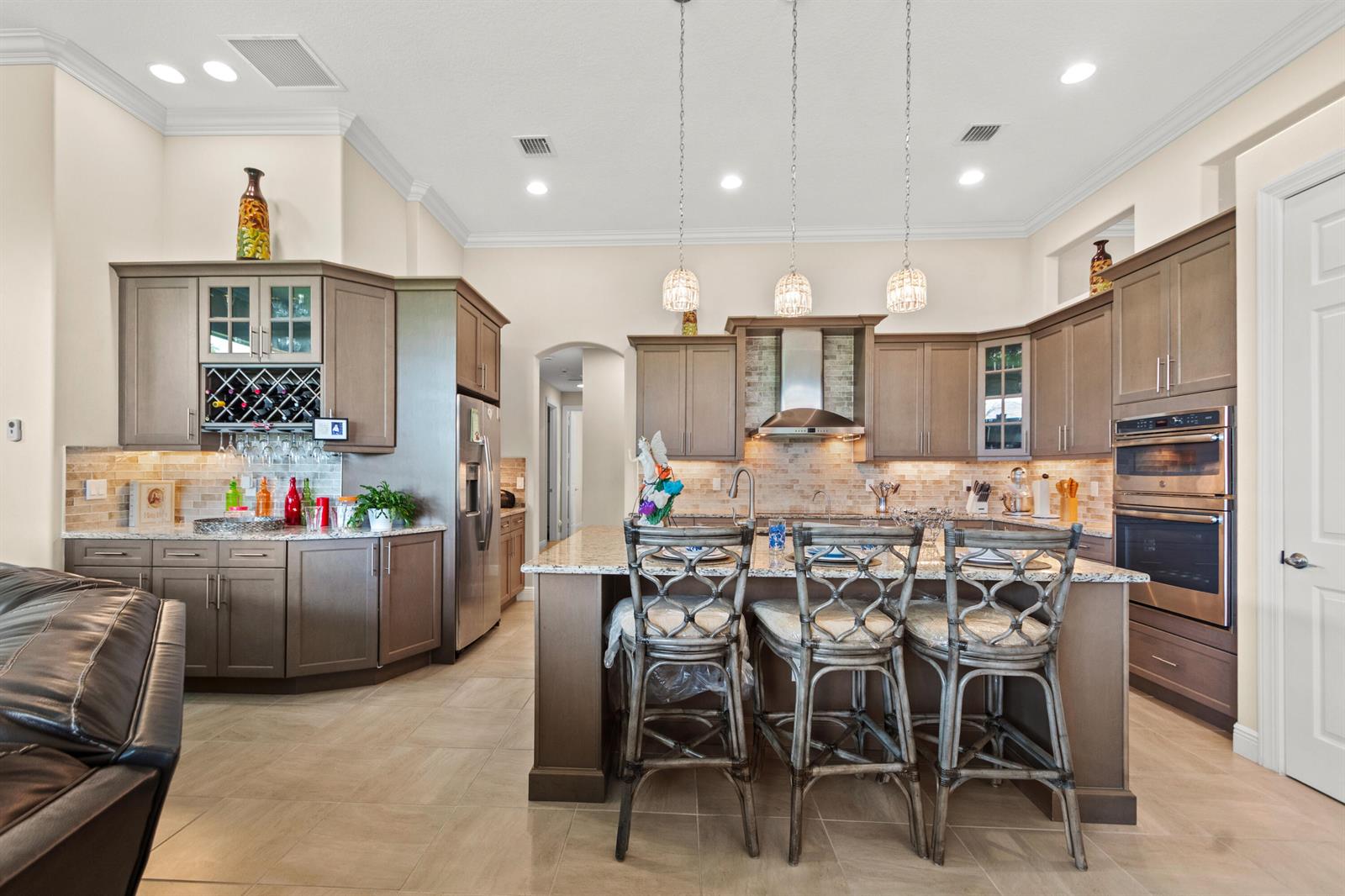 A kitchen features brown cabinetry, granite countertops, a central island with bar stools, and pendant lighting — 4405 65th Drive, Vero Beach FL 32967, VERO BEACH, FL