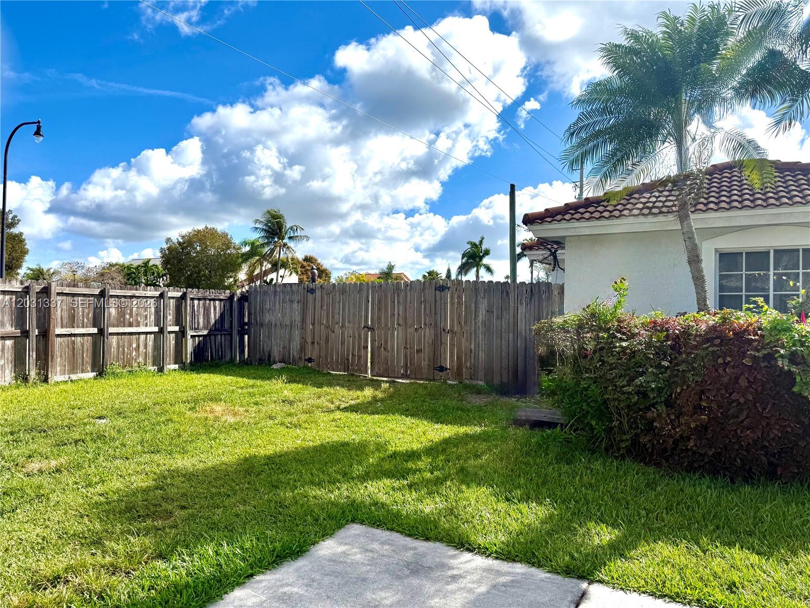 A grassy backyard features a wooden fence, a palm tree, and part of a house — 18003 SW 138th Ct, Miami FL 33177, MIAMI, FL