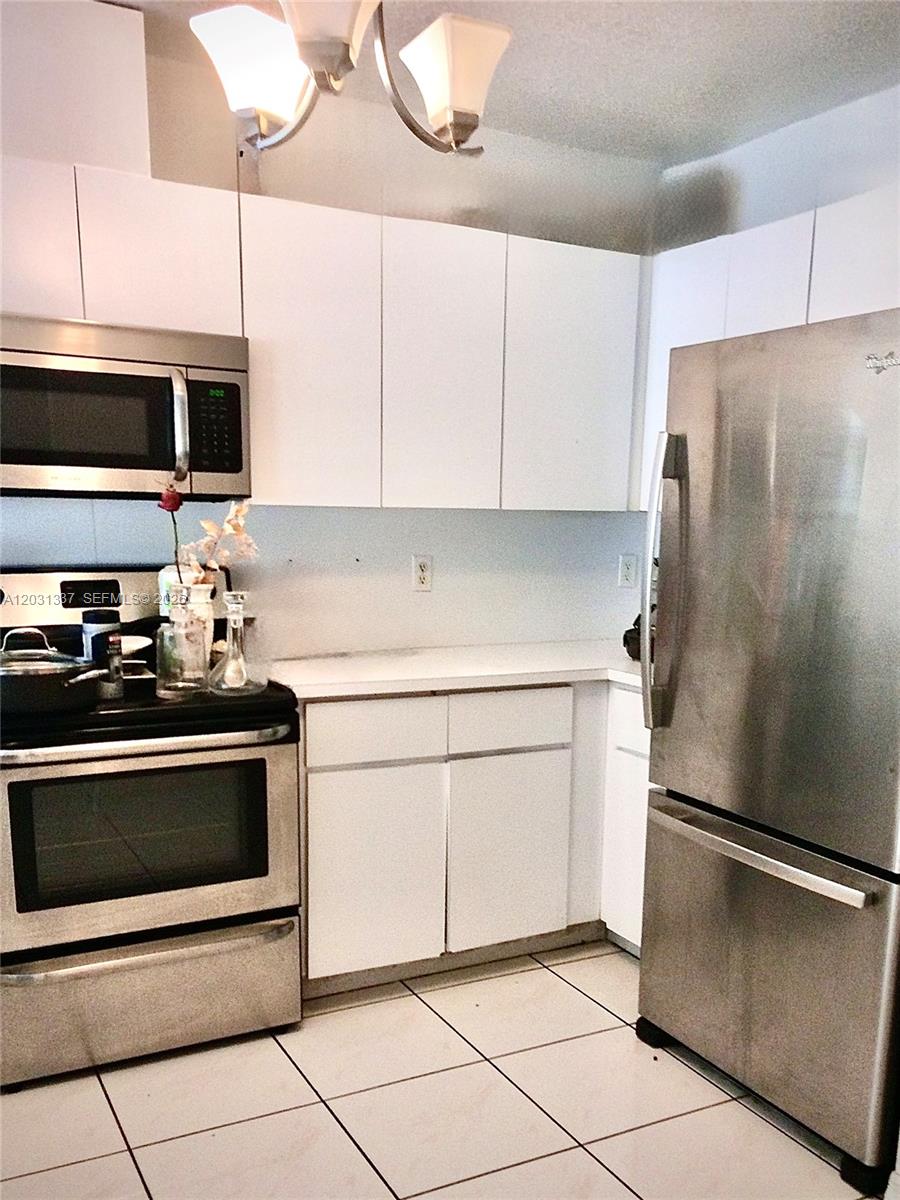 A kitchen features white cabinets, stainless steel appliances, and light-colored tile flooring — 18003 SW 138th Ct, Miami FL 33177, MIAMI, FL