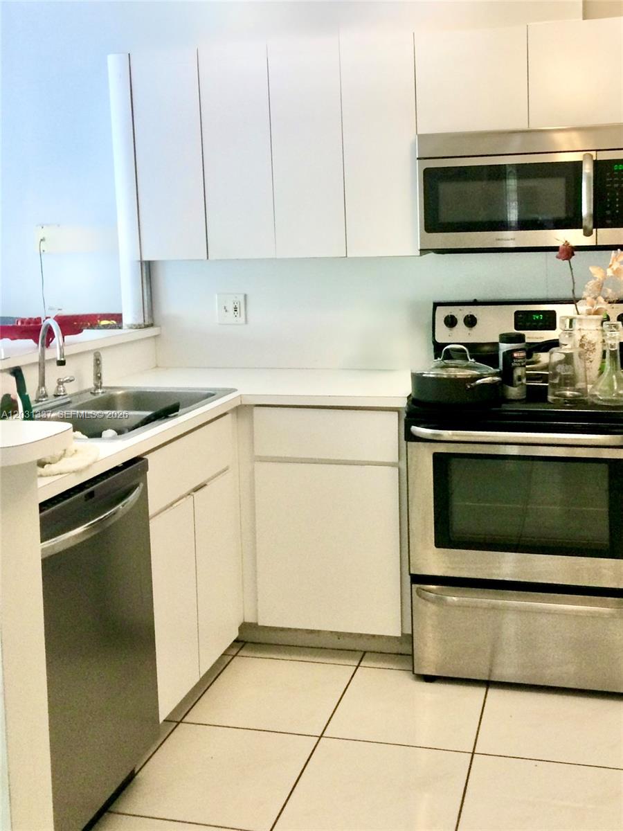 A kitchen features white cabinets, stainless steel appliances, and light-colored tile flooring — 18003 SW 138th Ct, Miami FL 33177, MIAMI, FL
