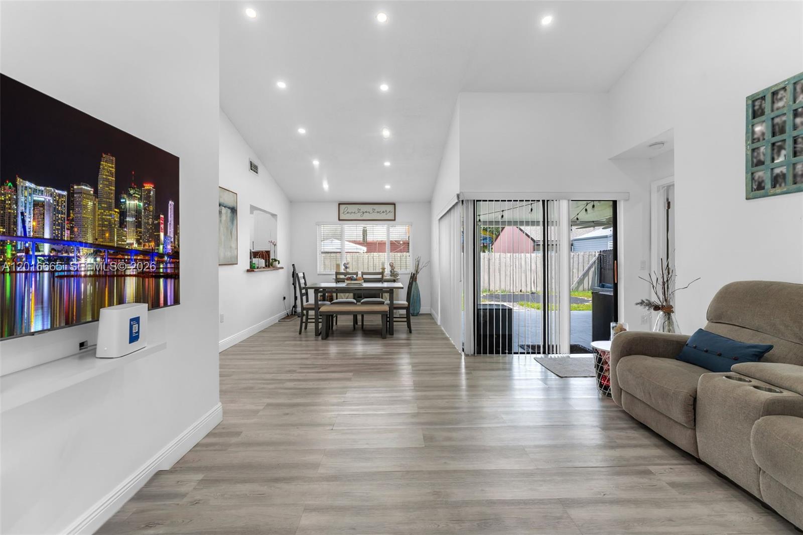 A living and dining area features light wood-look flooring, recessed lighting, and a sliding glass door — 12247 SW 203rd St, Miami FL 33177, MIAMI, FL
