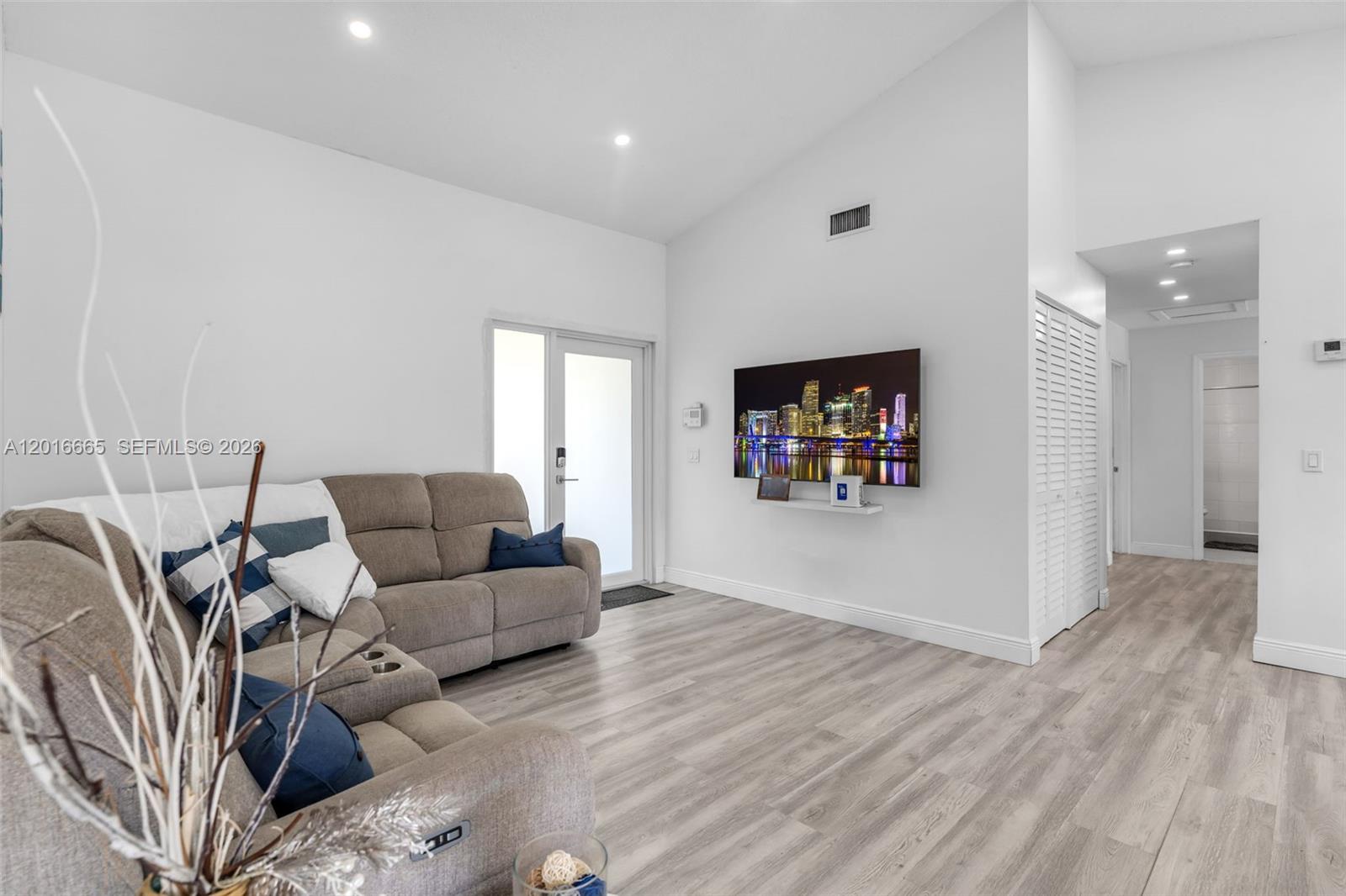 A living room features light wood-look flooring, a vaulted ceiling, and a wall-mounted television — 12247 SW 203rd St, Miami FL 33177, MIAMI, FL