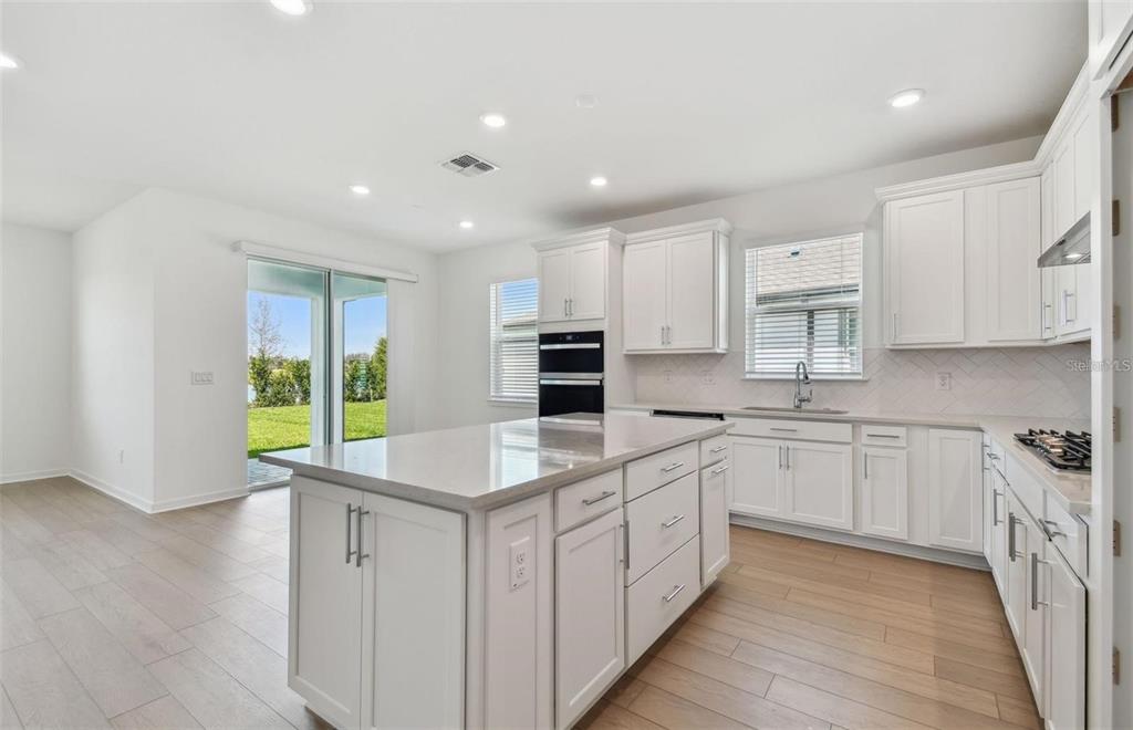 A modern kitchen features white cabinetry, a large central island, and light wood-look flooring — 6741 MICHAEL FAVOR WAY, WESLEY CHAPEL, FL