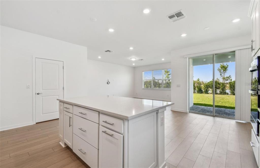 A bright kitchen with a white island, light wood-look flooring, and sliding glass patio doors — 6741 MICHAEL FAVOR WAY, WESLEY CHAPEL, FL
