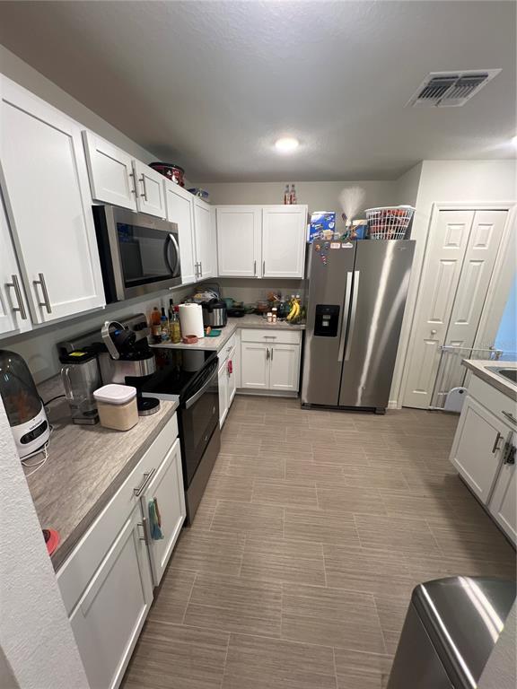 A kitchen features white cabinets, stainless steel appliances, and light-colored wood-look tile flooring — 46 WILLOW LANE, KISSIMMEE, FL