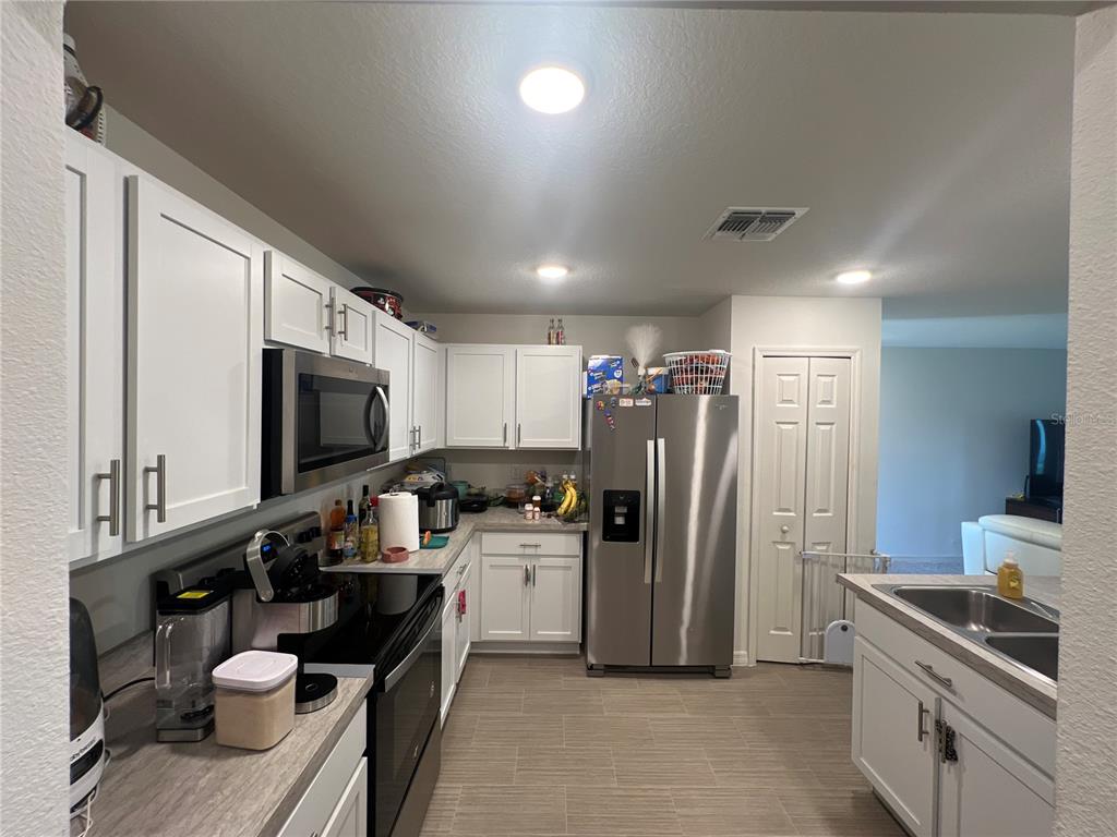 A kitchen features white cabinets, stainless steel appliances, and light-colored tile flooring — 46 WILLOW LANE, KISSIMMEE, FL