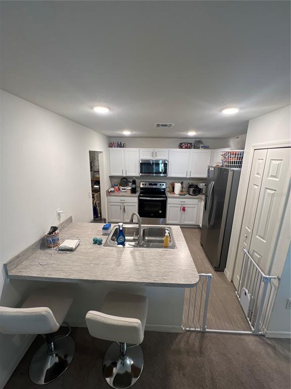 A kitchen features white cabinets, stainless steel appliances, a breakfast bar, and a baby gate — 46 WILLOW LANE, KISSIMMEE, FL