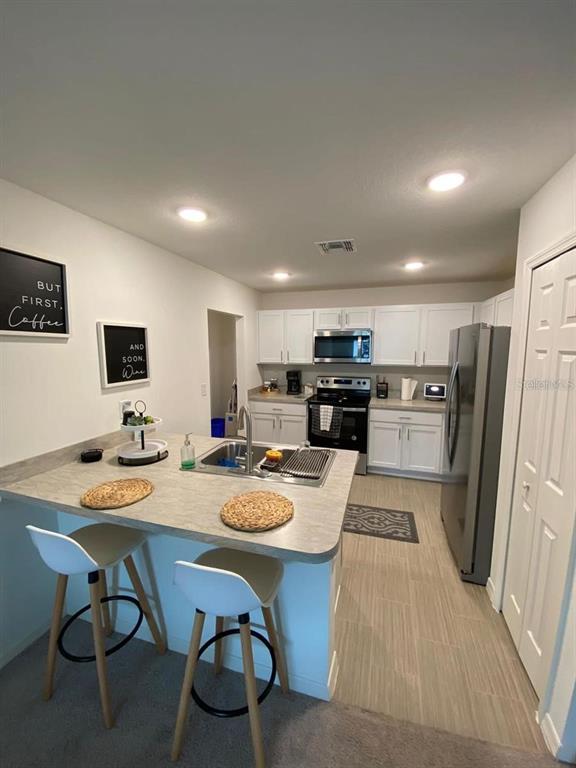 A kitchen features white cabinets, stainless steel appliances, a breakfast bar, and light-colored flooring — 46 WILLOW LANE, KISSIMMEE, FL