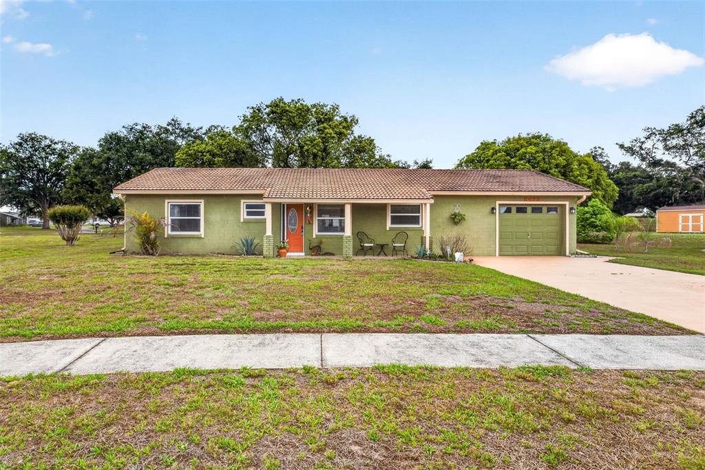 A single-story green house with a tiled roof, orange front door, and attached garage — 8429 JACQUELINE COURT, ZEPHYRHILLS, FL