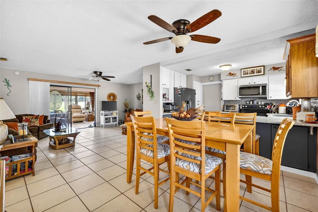 An open-concept dining area and living room featuring tile floors and wooden furniture — 8429 JACQUELINE COURT, ZEPHYRHILLS, FL