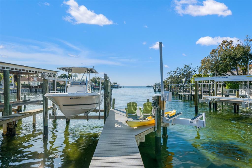 A boat lift with a boat and a dock with chairs and kayaks on water — 2605 S BEACH DRIVE, TAMPA, FL
