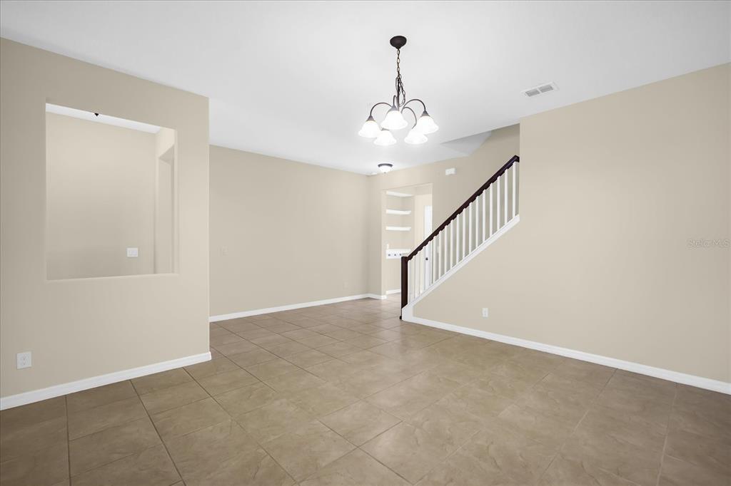 An empty room with beige walls, tile flooring, a chandelier, and a staircase — 8943 HILDRETH AVENUE, ORLANDO, FL