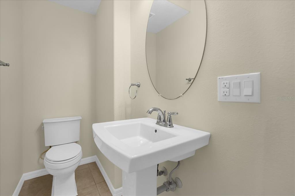 A small bathroom features a pedestal sink, a toilet, and an oval wall mirror — 8943 HILDRETH AVENUE, ORLANDO, FL