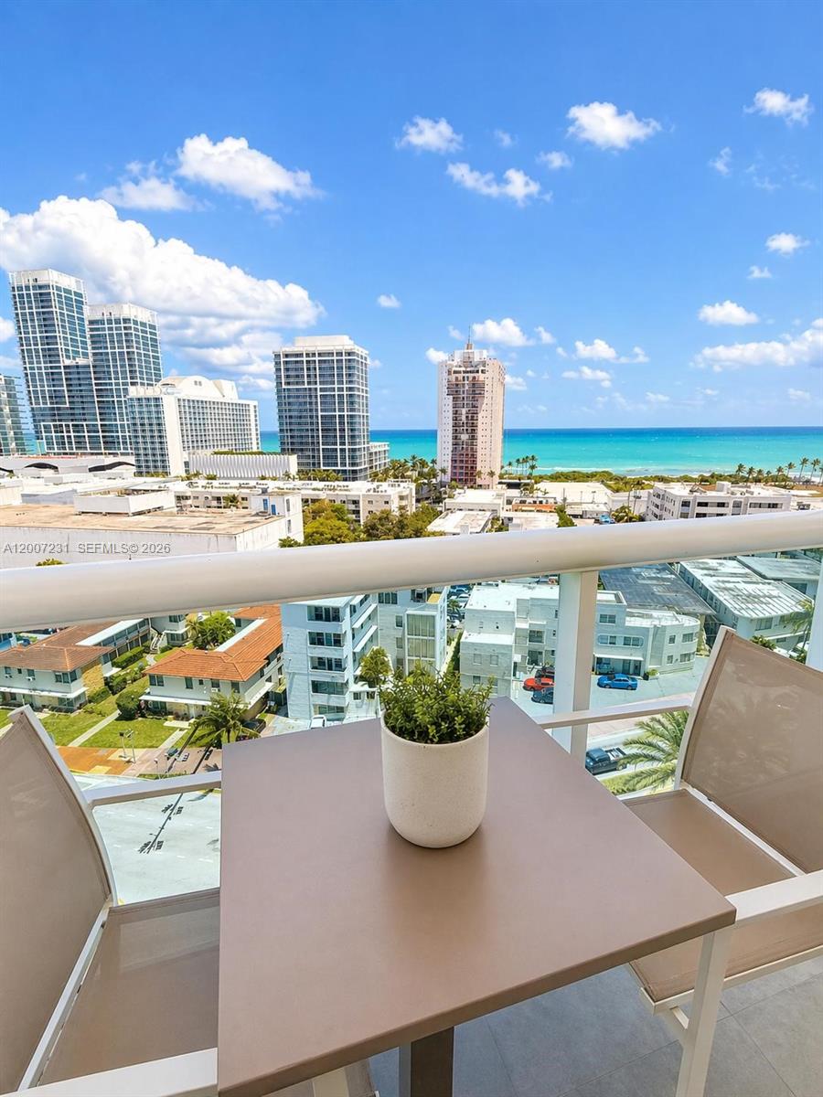 A balcony with a small table and chairs overlooks a city skyline and the ocean — 6770 Indian Creek Dr # 12T, Miami Beach FL 33141, MIAMI BEACH, FL