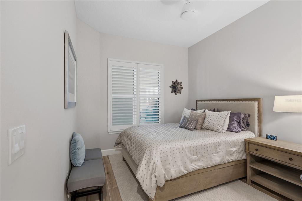 A bedroom features a bed with a wooden frame, a gray bench, and plantation shutters — 807 S ATLANTIC AVENUE UNIT 303, NEW SMYRNA BEACH, FL