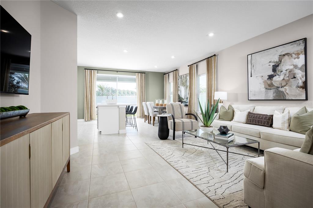 An open-concept living and dining area features tile flooring, neutral walls, and a large sofa — 20474 LOU ANGELA LANE, LUTZ, FL