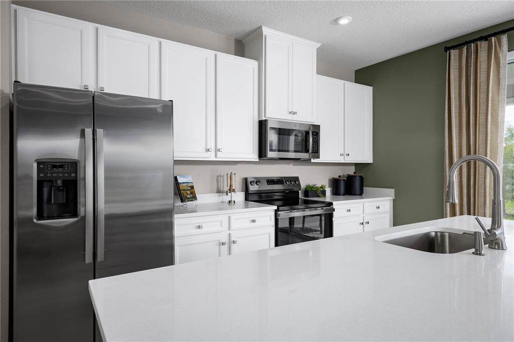 A modern kitchen features white cabinets, stainless steel appliances, and a white quartz island countertop — 20474 LOU ANGELA LANE, LUTZ, FL