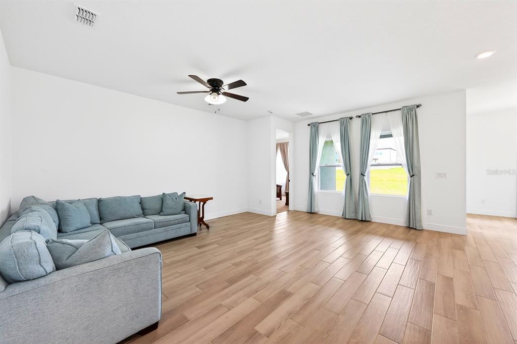 A living room with light wood-look tile flooring, a blue sectional sofa, and two windows — 1369 STERLING POINTE DRIVE, DELTONA, FL