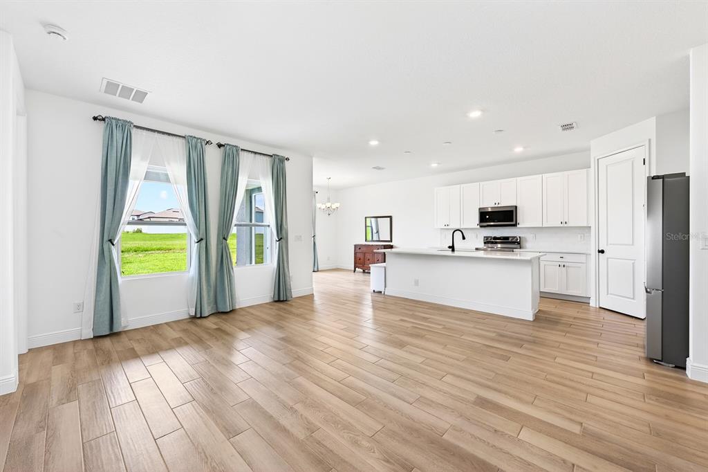 An open-concept kitchen and living area features white cabinetry, a central island, and wood-look flooring — 1369 STERLING POINTE DRIVE, DELTONA, FL
