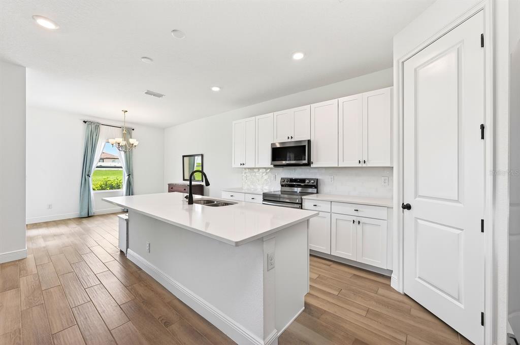 A modern kitchen features white cabinets, a large island with a sink, and wood-look flooring — 1369 STERLING POINTE DRIVE, DELTONA, FL