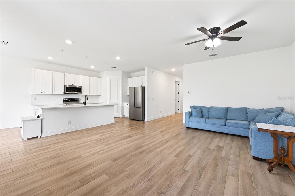 An open-concept kitchen and living area features white cabinetry, stainless appliances, and blue sectional sofa — 1369 STERLING POINTE DRIVE, DELTONA, FL