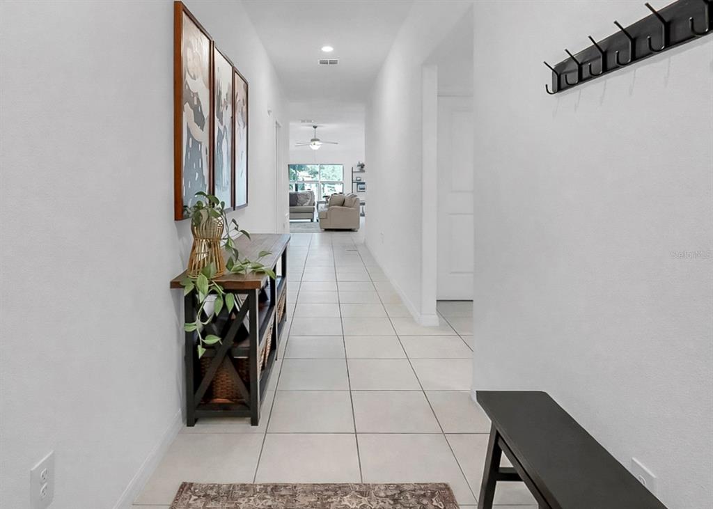 A bright hallway with light tile flooring leads toward a living room with a ceiling fan — 13256 GREAT PLAINS DRIVE, RIVERVIEW, FL