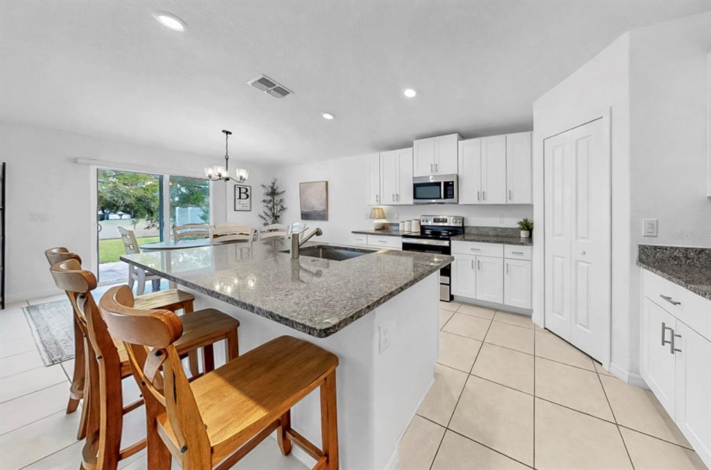 A kitchen features white cabinets, granite countertops, a central island with bar seating, and tile flooring — 13256 GREAT PLAINS DRIVE, RIVERVIEW, FL