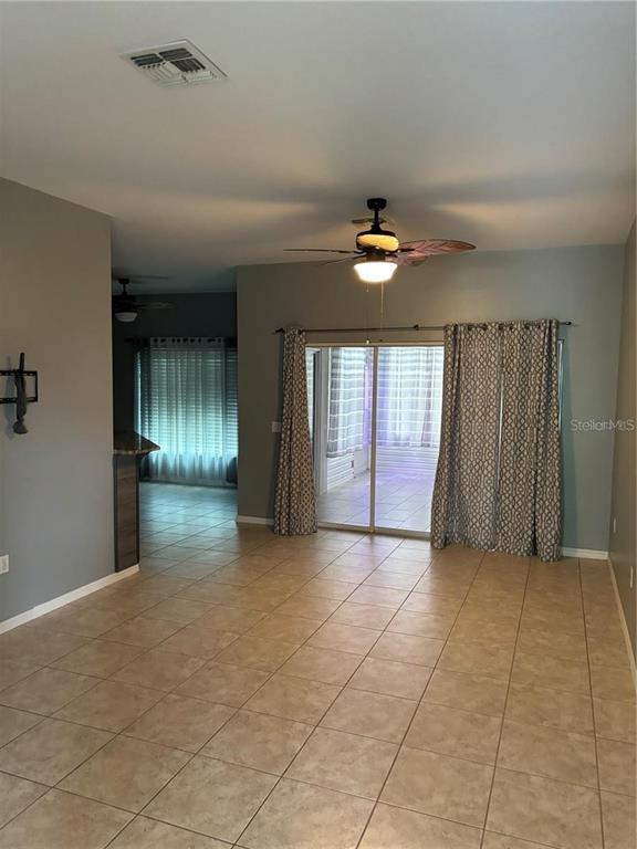 A living room with tile flooring, a ceiling fan, and sliding glass doors with curtains — 284 LAKE CASSIDY DRIVE, POINCIANA, FL