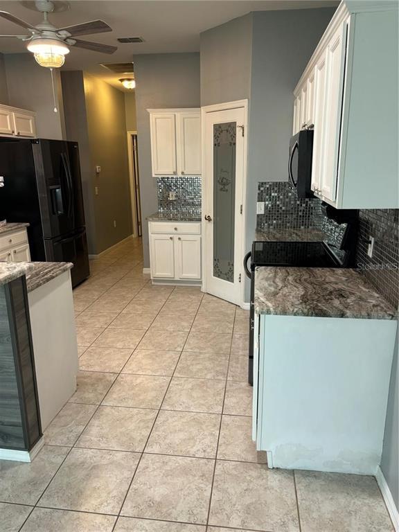 A kitchen features white cabinets, dark granite countertops, a mosaic backsplash, and tile flooring — 284 LAKE CASSIDY DRIVE, POINCIANA, FL
