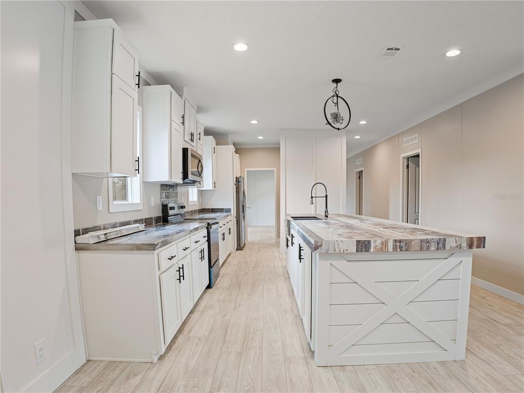 A kitchen features white cabinetry, a farmhouse-style island, and wood-look countertops — 45 KELLY RIDGE ROAD, FROSTPROOF, FL