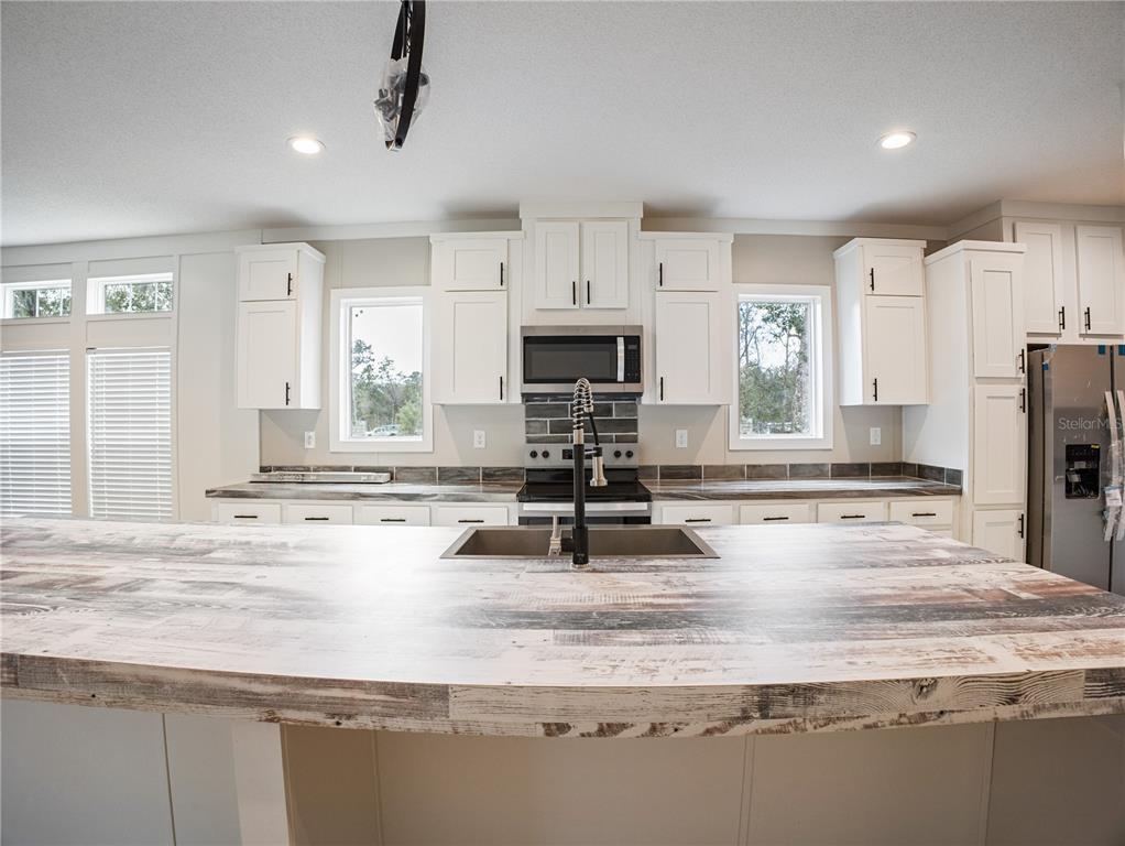 A kitchen features white cabinets, a large island with a rustic wood-look countertop, and windows — 45 KELLY RIDGE ROAD, FROSTPROOF, FL