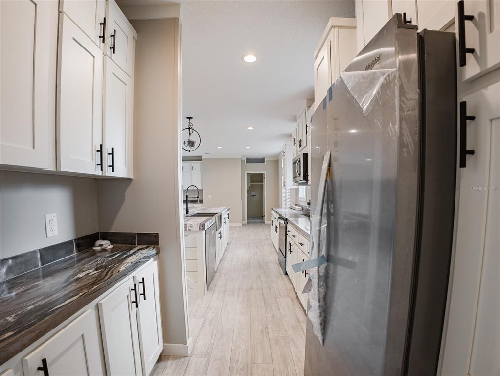 A kitchen features white cabinets, dark marble-patterned countertops, stainless steel appliances, and wood-look flooring — 45 KELLY RIDGE ROAD, FROSTPROOF, FL